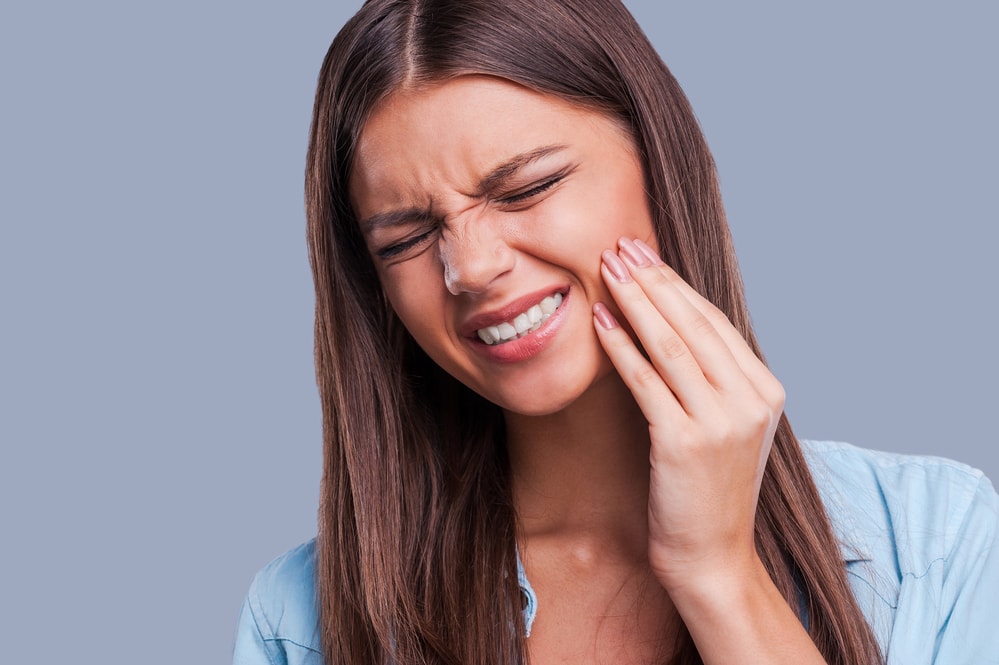 Suffering from toothache. Beautiful young woman suffering from toothache while standing against grey background