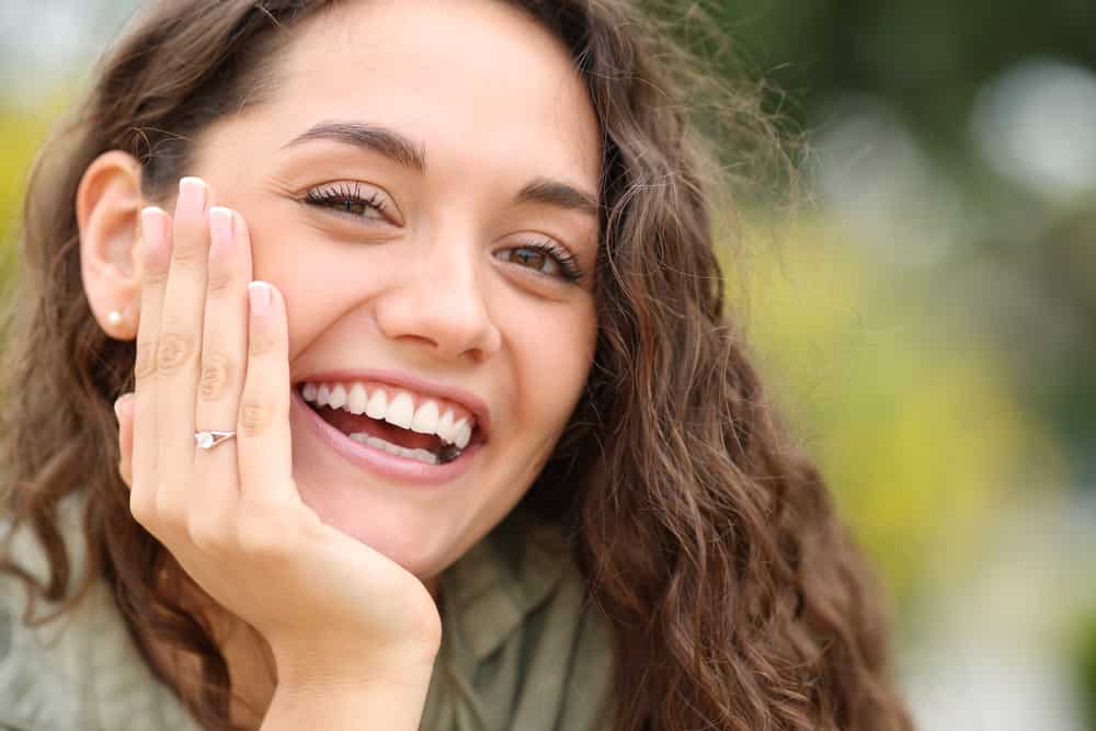 Happy woman smiling at camera showing engagement ring in a park